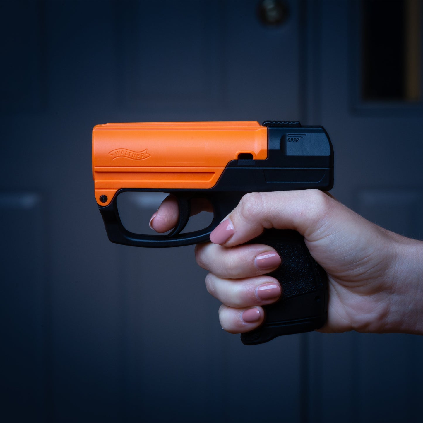 Someone holding Aim and Fire Pepper Gel with Trigger and Grip Deployment – pistol-style pepper gel launcher featuring a 15-foot range, 13 bursts per cartridge, and a grip safety to prevent accidental discharge, at night.