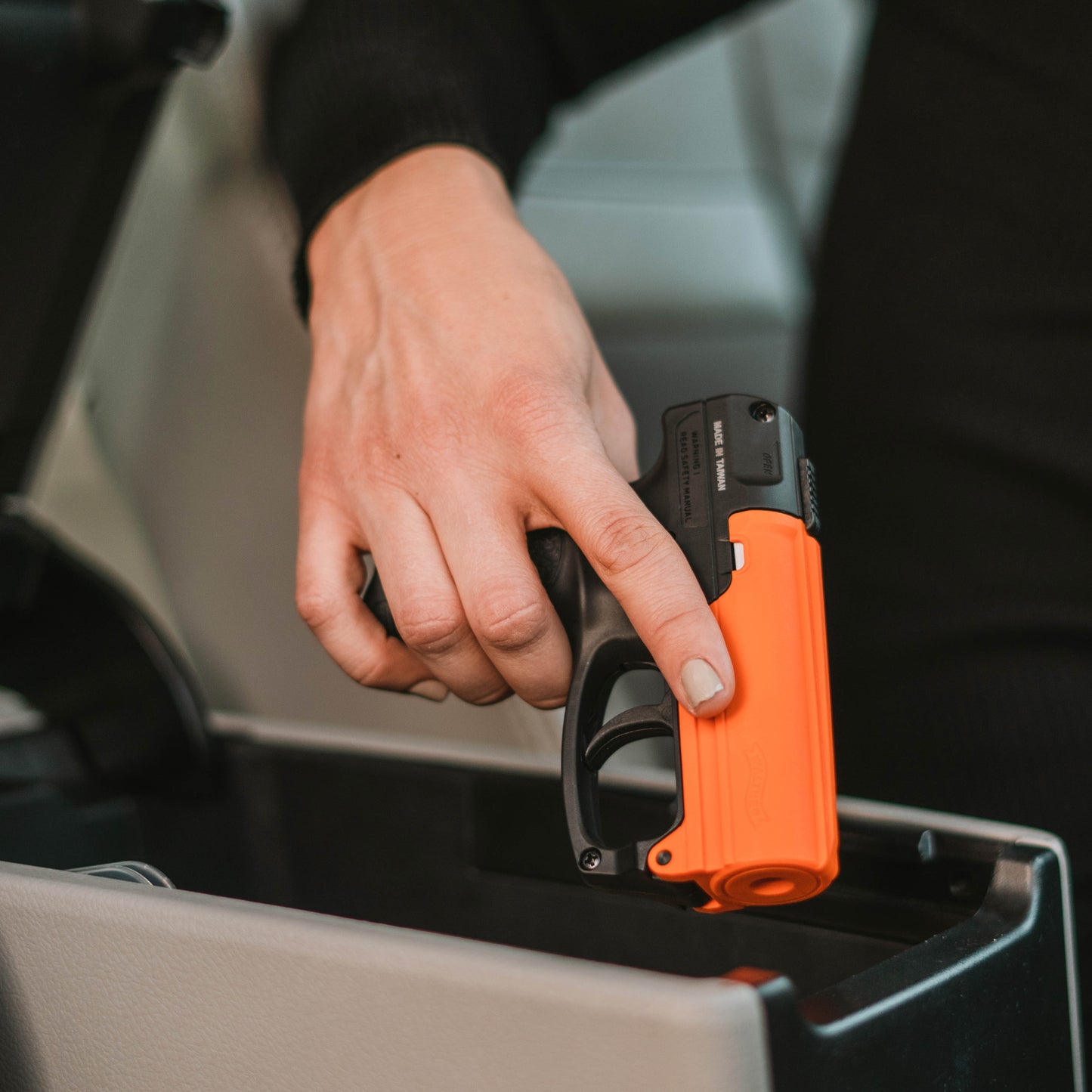 Someone holding Aim and Fire Pepper Gel with Trigger and Grip Deployment – pistol-style pepper gel launcher featuring a 15-foot range, 13 bursts per cartridge, and a grip safety to prevent accidental discharge, inside a car.