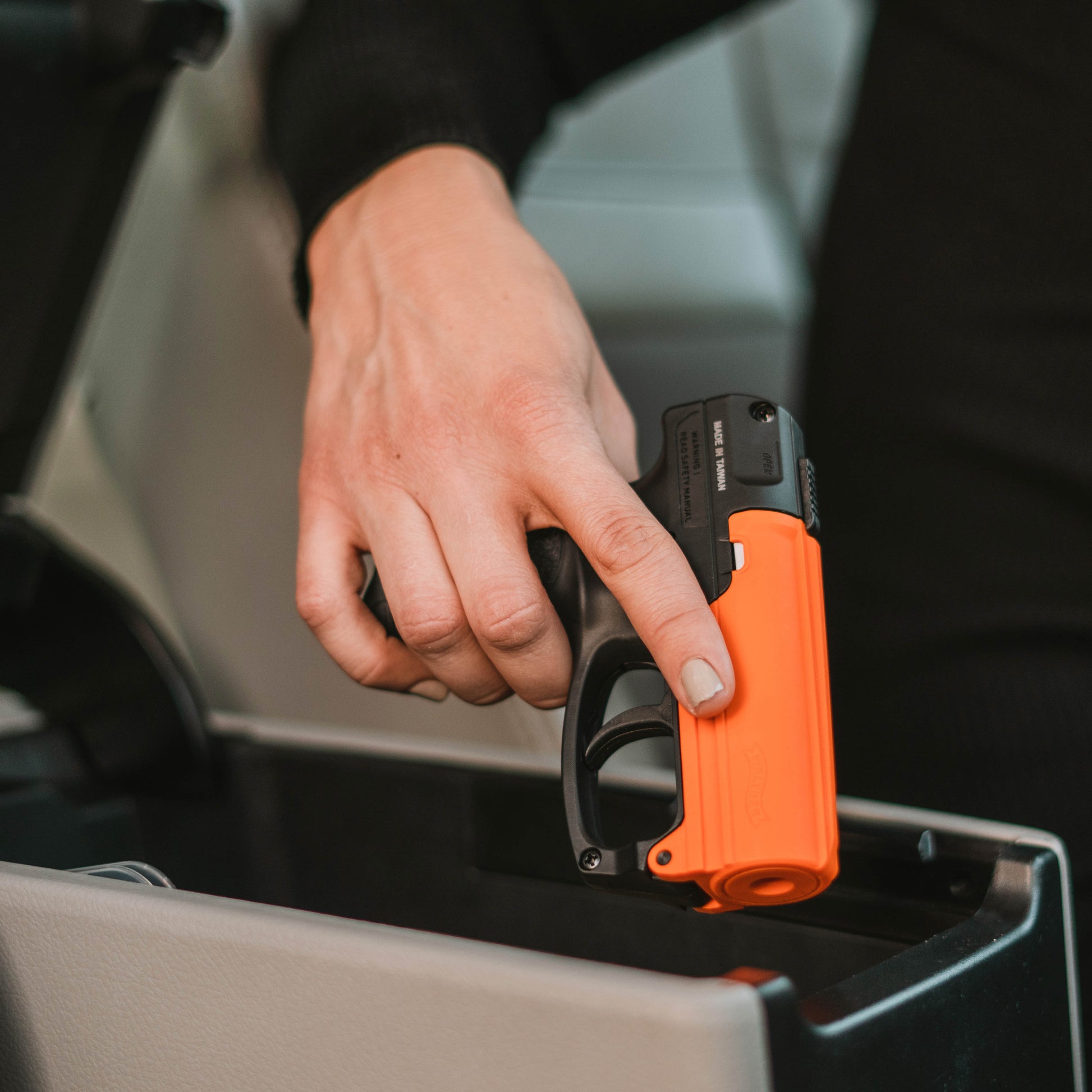 Someone holding Aim and Fire Pepper Gel with Trigger and Grip Deployment – pistol-style pepper gel launcher featuring a 15-foot range, 13 bursts per cartridge, and a grip safety to prevent accidental discharge, inside a car.