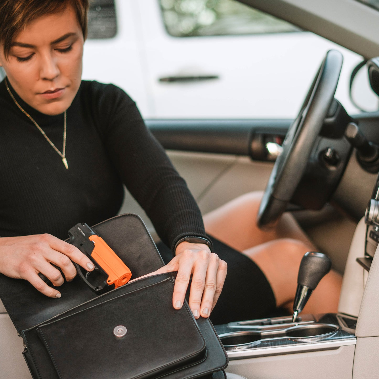 Someone packing into purse an Aim and Fire Pepper Gel with Trigger and Grip Deployment – pistol-style pepper gel launcher featuring a 15-foot range, 13 bursts per cartridge, and a grip safety to prevent accidental discharge, inside a car.