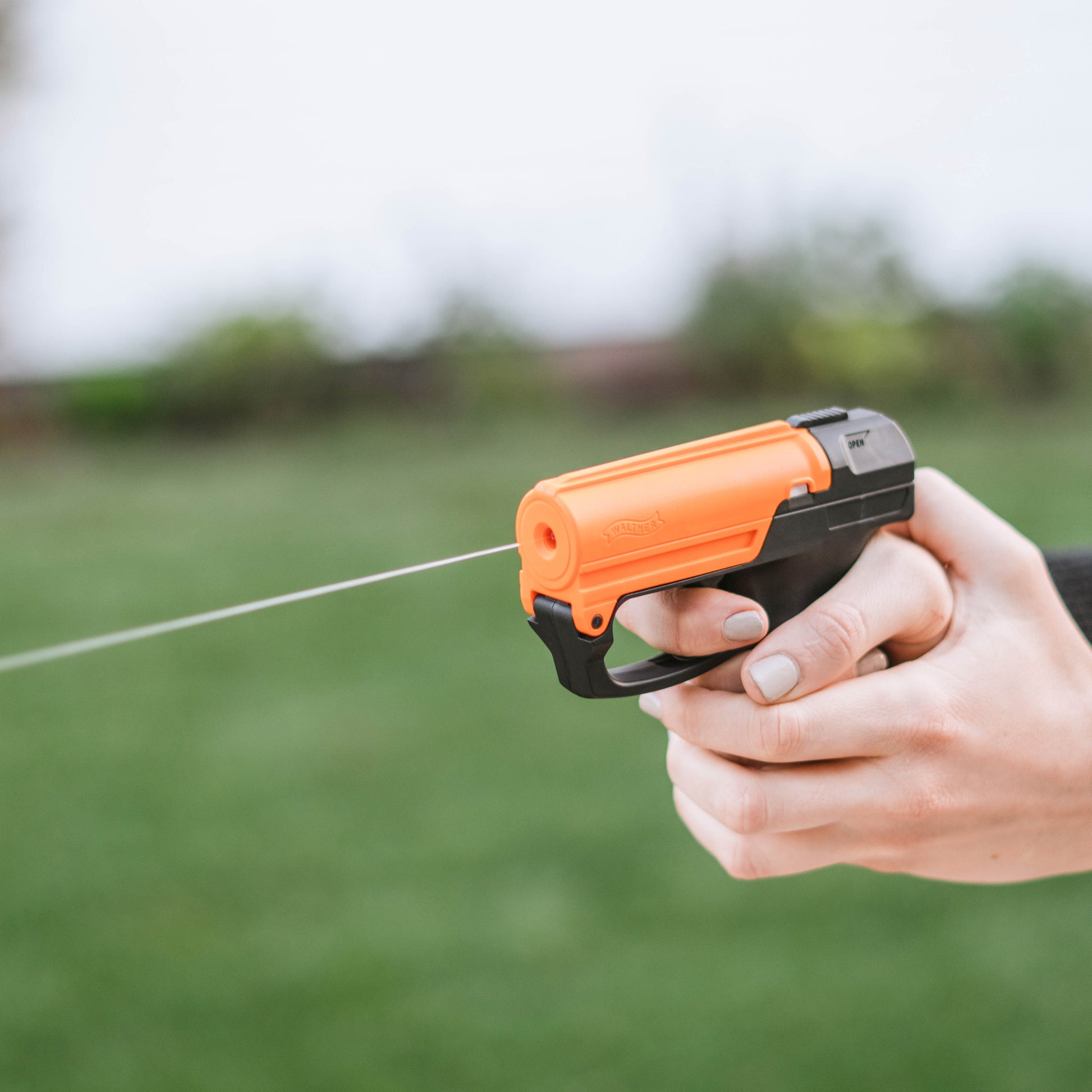 Someone firing Aim and Fire Pepper Gel with Trigger and Grip Deployment – pistol-style pepper gel launcher featuring a 15-foot range, 13 bursts per cartridge, and a grip safety to prevent accidental discharge, in open space.