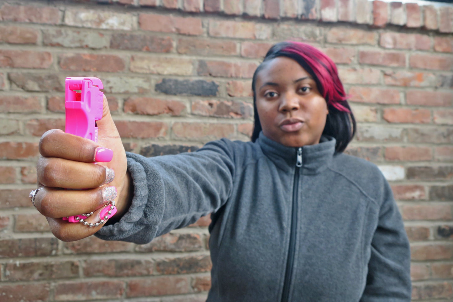 Someone holding Mace Pocket Model Stream Pepper Spray – compact self-defense spray with a focused stream pattern delivering up to 10 ft of range, flip-top safety cap, finger-grip design, and UV dye for attacker identification, with wall background.