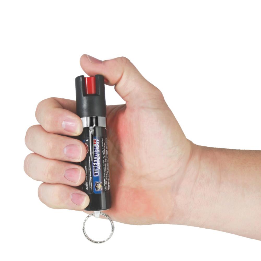 Someone holding Streetwise 18 Pepper Spray 0.75 oz Keyring & Clip - compact self-defense spray on white background.